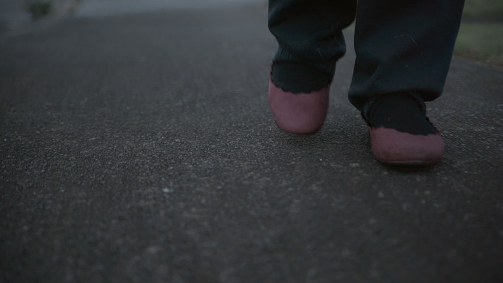 Reconstruction of Katrina in blue trackpants and wearing burgundy slip on shoes.