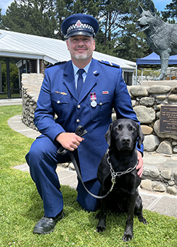 Senior Constable Lyal Bayliss crouching down next to detector dog Luther.