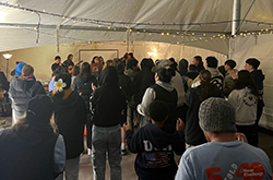 Photo from behind of people watching live music in the 40 Hour Challenge tent.