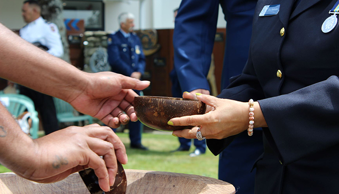 A close up on an officer's hands as they fill a kava bowl and pass it to someone.