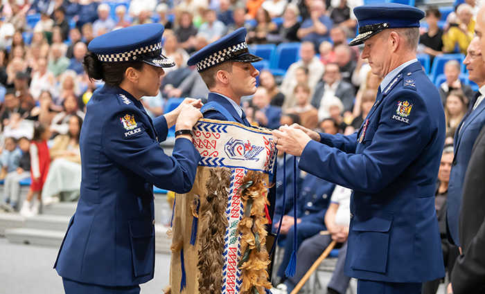 Constable David Cramp, who came top of his wing and won the Firearms Award, receives the RNZPC Korowai from Commissioner Coster.