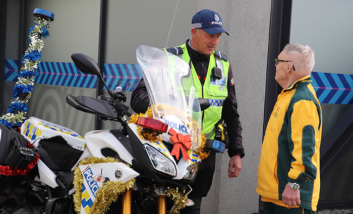 Senior Const Johnny McGrail speaking to an athlete next to a police motorcycle covered in Christmas decorations..