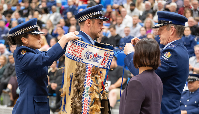 Police Commissioner Andrew Coster tying the Police korowai around Constable Christian Merten's shoulders as Police Minister Ginny Andersen looks on.