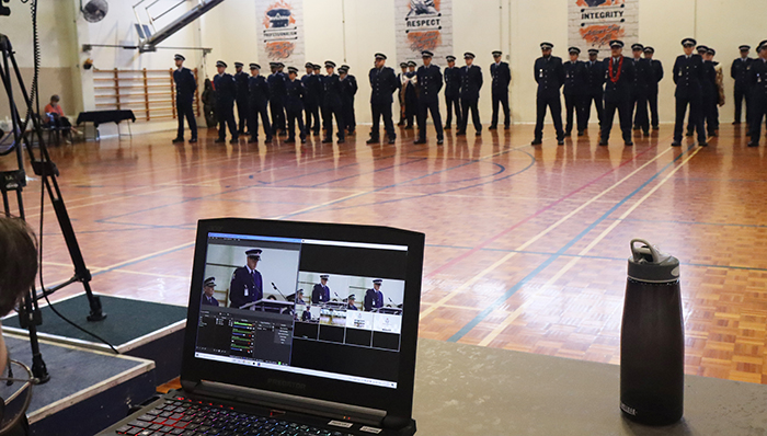 The ceremony was livestreamed to family and friends - the screen shows Leadership Award winner Constable Mike Robertson speaking to the audience.