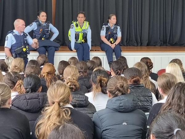 Officers leaning against a stage in an assembly hall chatting to Gisborne Girls' High School students.