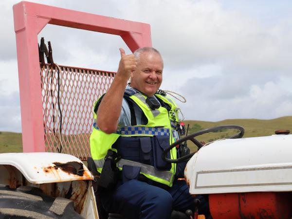 Senior Constable Dean Fawcett waving at the camera from a tractor pulling a boat to shore. 