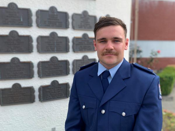 Constable Jonty Boyd in front of the wall of remembrance at the Royal New Zealand Training College 