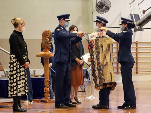 Patron Linda Clark and Minister Williams watch as Commissioner Coster ties the korowai for Constable Dylan Buttar-Scurr.