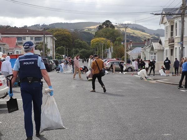 Wide shot of Castle Street showing a police officer carrying a spade and bag of rubbish and students cleaning up in the distance