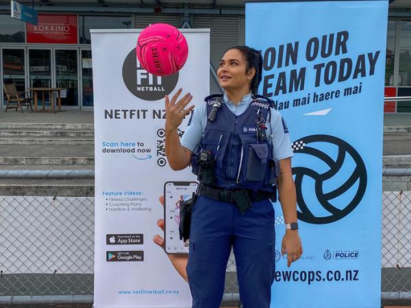 Eseta in police uniform throwing a pink netball in the air in front of a 'Join our team today' newcops recruitment banner.