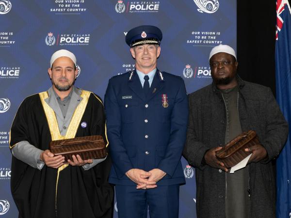 Commissioner Coster standing between Imams Gamal Fouda, left, and Abdul Alabi Lateef as they each hold the waka huia.