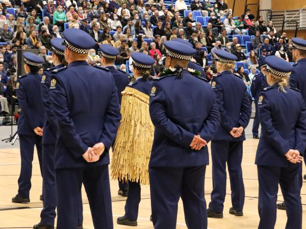 View of the backs of some the recruits as they stand facing their families and friends in the audience at their graduation.