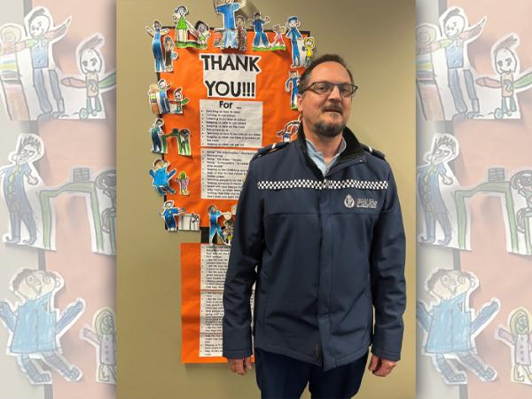 Constable Marcus Rudge standing in front of the thank you poster from the students.