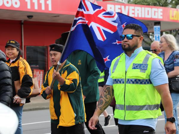 Officer walks alongside an athlete who is waving the New Zealand flag.