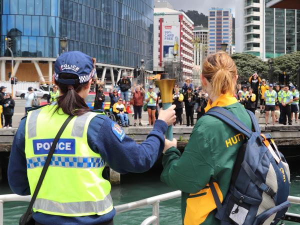 Officer and athlete on the Lady Liz holding the torch of hope together looking to the wharf where other athletes are cheering.