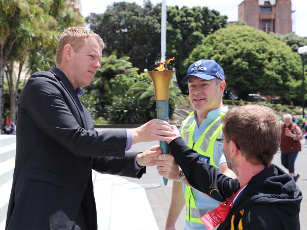 Commissioner of Police and an athlete pass the torch on to the Minister of Police on the steps of parliament.