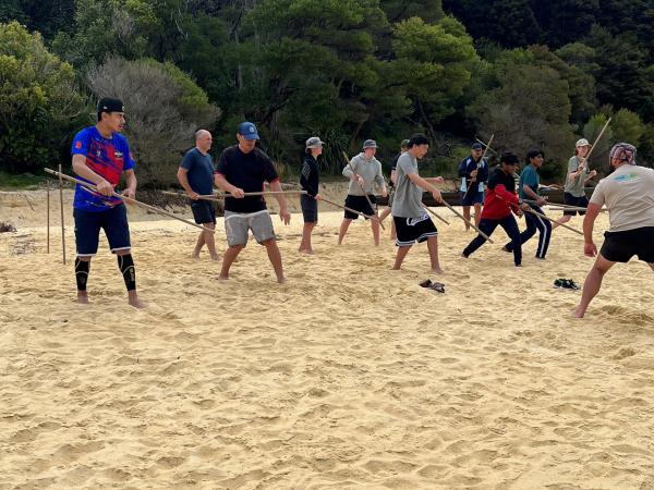 The group learn the ancient art of Taiaha on the golden sands of Anchorage.