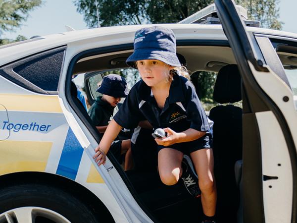 A young student jumping out of a police car. 