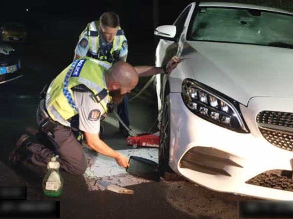Two officers with the car jacked up, sliding the tray under one of its wheels. 