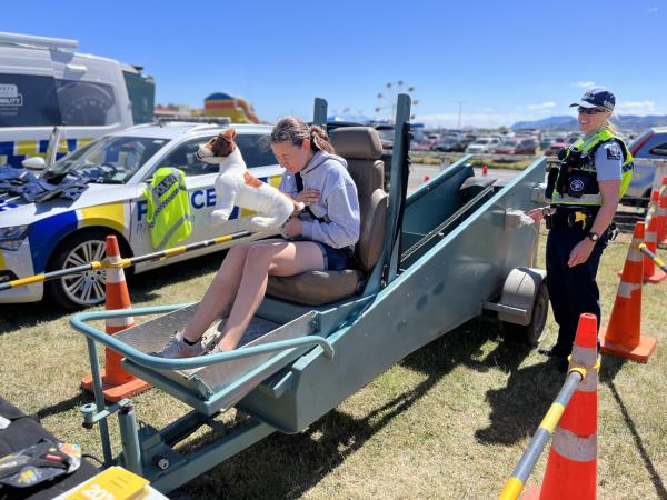Senior Constable Mel Allen operates the seat belt simulator, with someone sitting on it holding a toy dog.