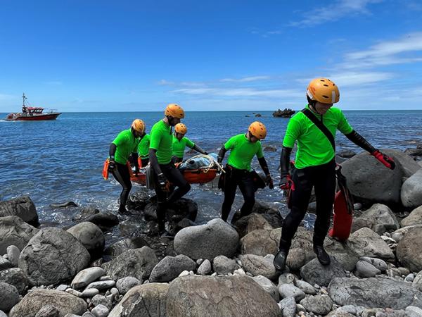 Six team members carrying a stretcher over rocks after recovery the 'dummy' from the water.