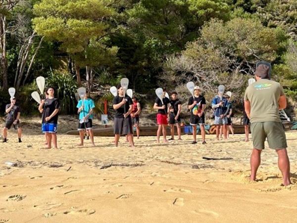 A back shot of one of the instructors standing in front of a group of the boys shwoing them how to hold and use their paddles. 