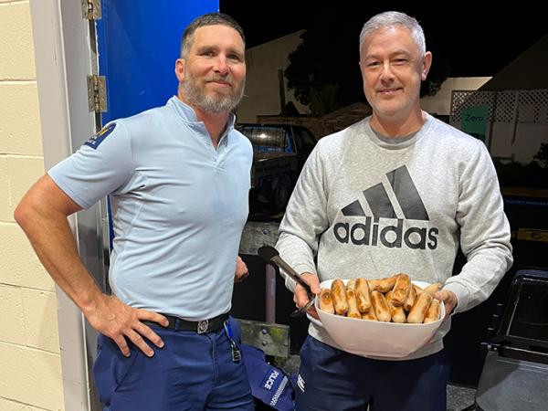 Senior Constable Paul Bascand in uniform standing next to Constable Rodney Berg who's holding the barbecue sausages.