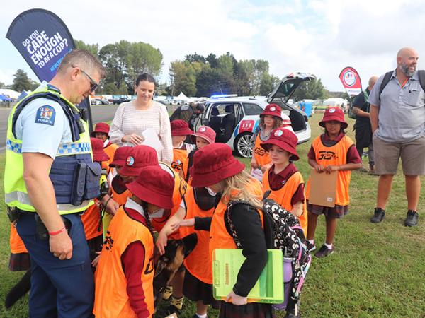 Children in ornage high-vis vests patting police puppy Iha. 