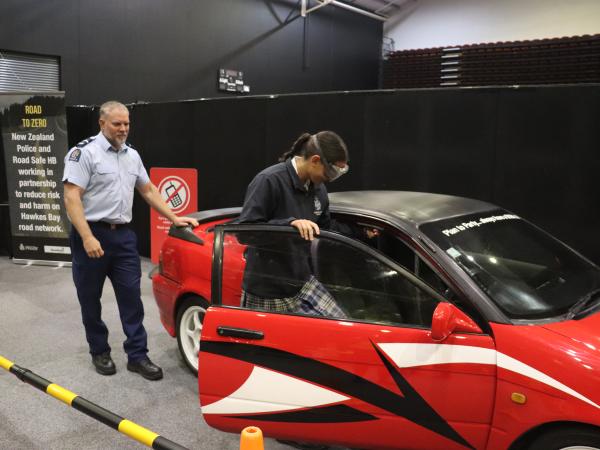 Senior Constable Cam Burn helps students experience attempting to get in a car while they're wearing fatal vision googles.