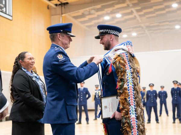 Commissioner Andrew Coster ties the Police korowai onto the First in Wing, Constable Kieran Carter.