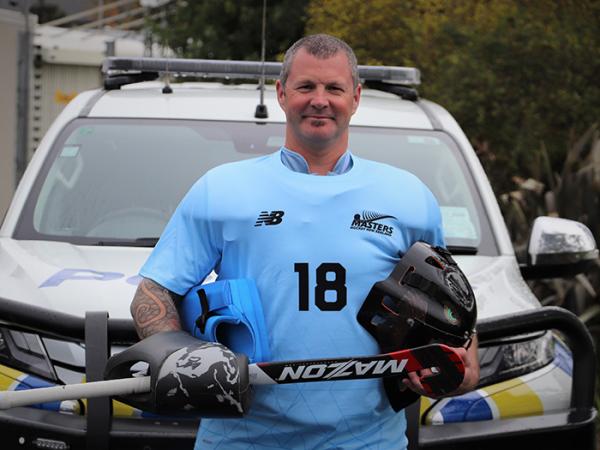 Constable Sam Davidson in his New Zealand hockey kit standing in front of a police car.