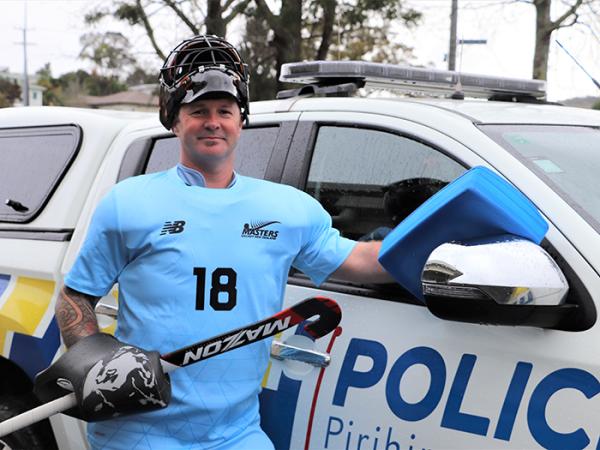 Constable Sam Davidson in his New Zealand hockey kit standing beside a police car.