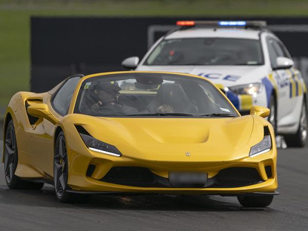 A yellow Ferrari on the racetrack with a police car following behind. 